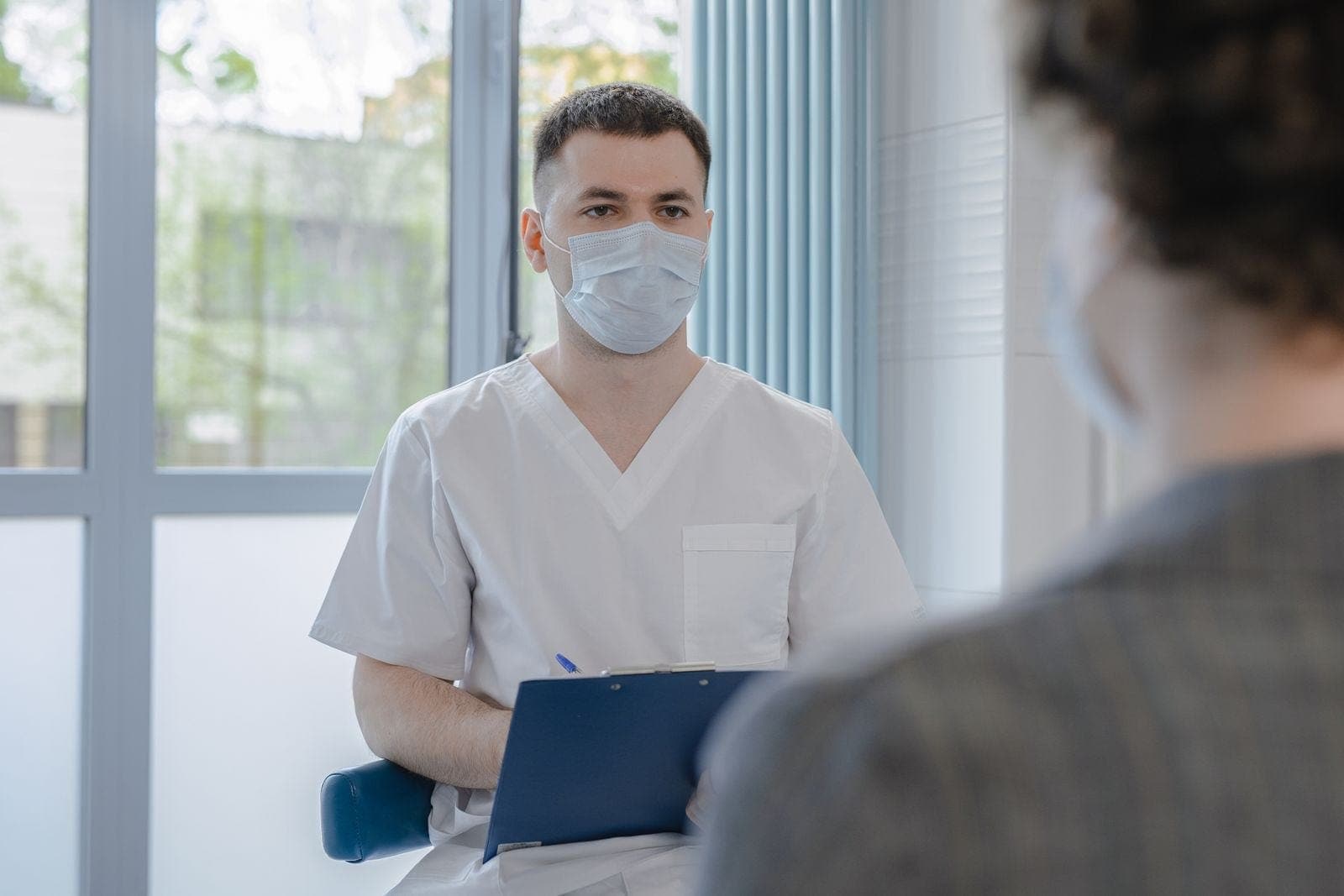 A healthcare professional holding a clipboard and speaking with a patient