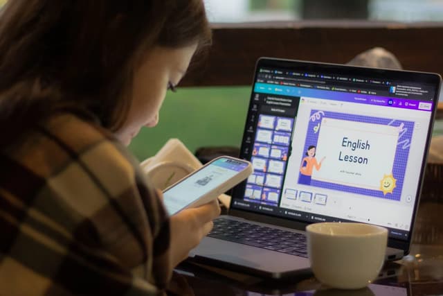 A person studying an English lesson on a laptop while holding a phone