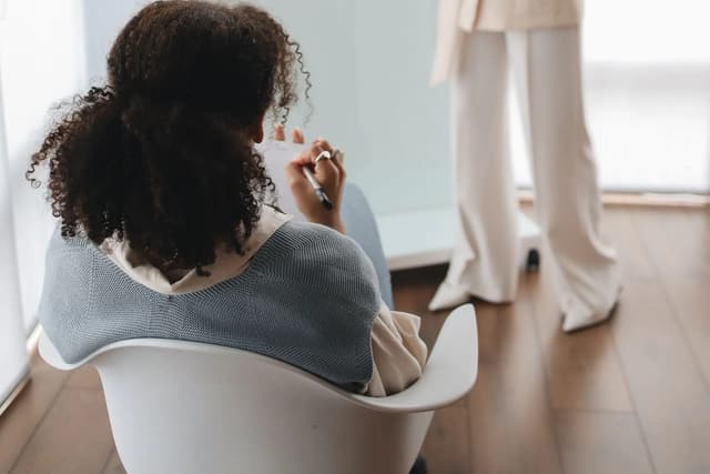 A seated woman listening to a standing instructor in a bright room