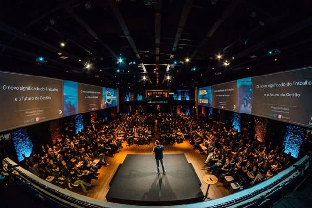 A speaker standing onstage before a large audience in an auditorium