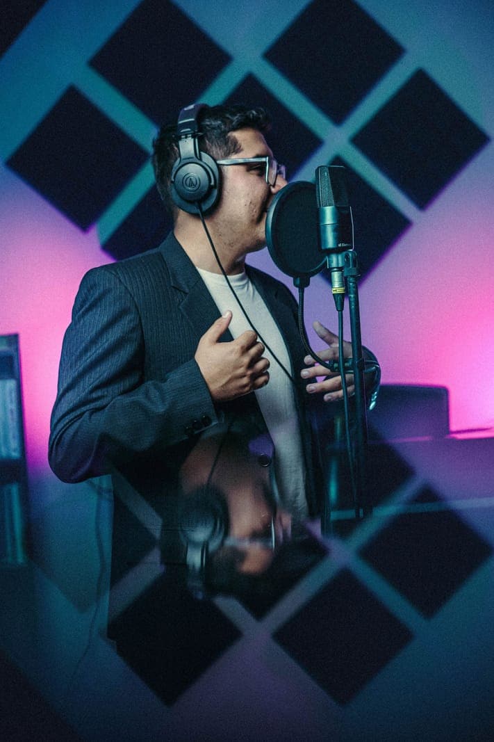 A man wearing headphones and gesturing at a studio microphone