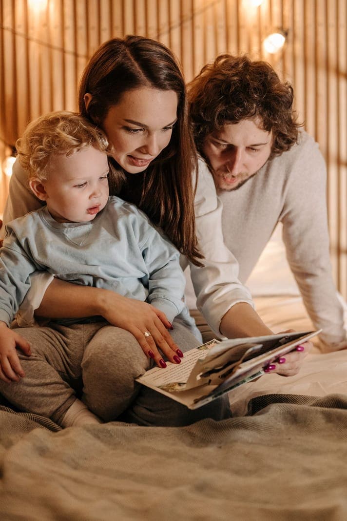 Two adults and a young child reading a picture book together