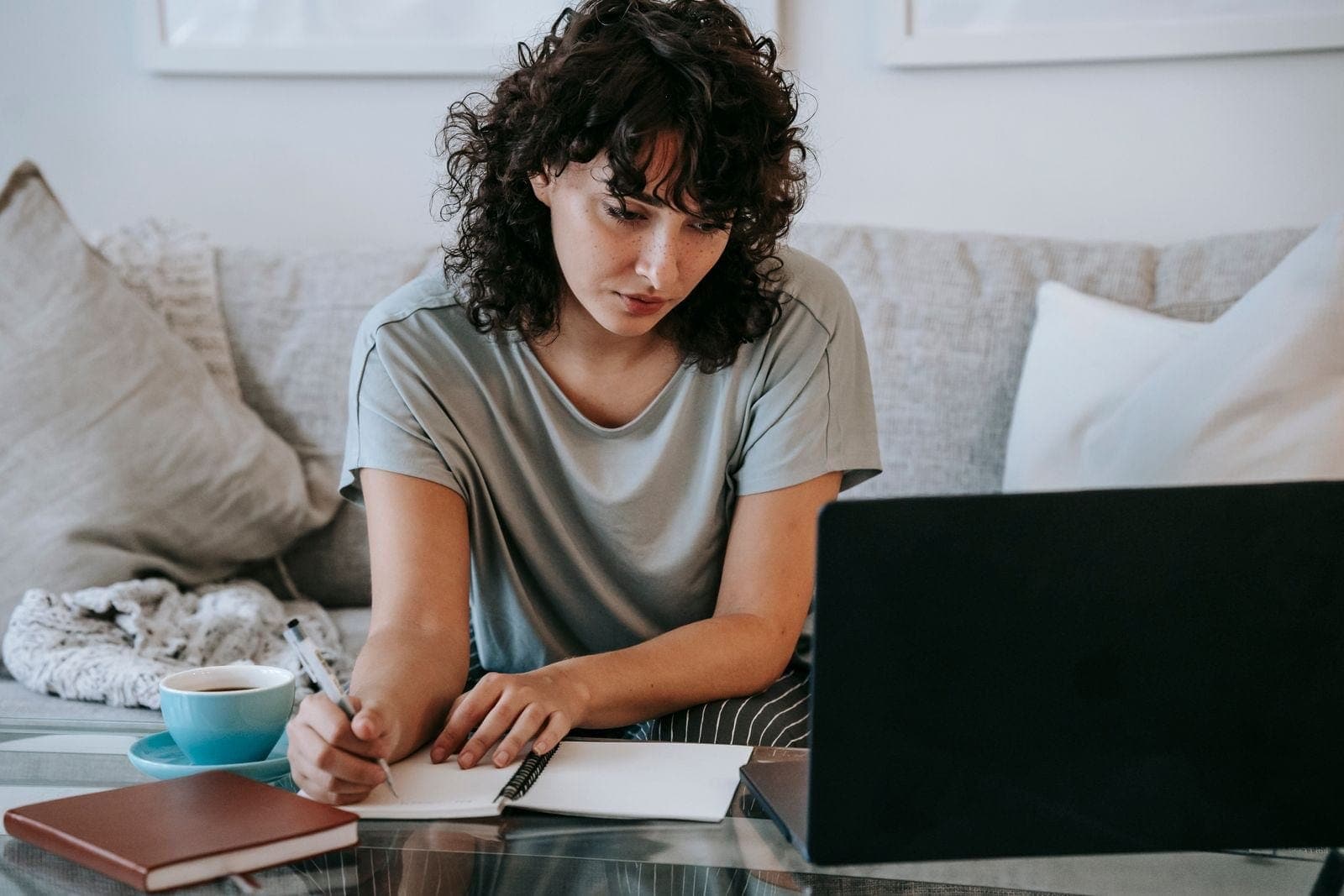 Serious young lady writing in notebook during online studies on laptop at home