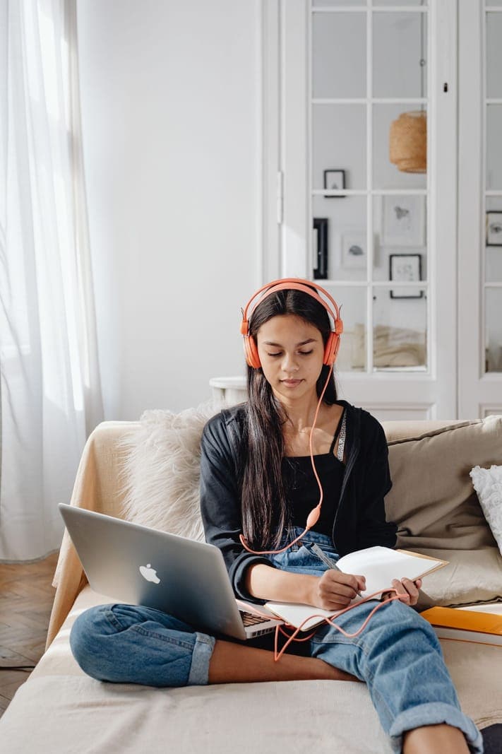 Woman Writing on a Notebook While Using Laptop