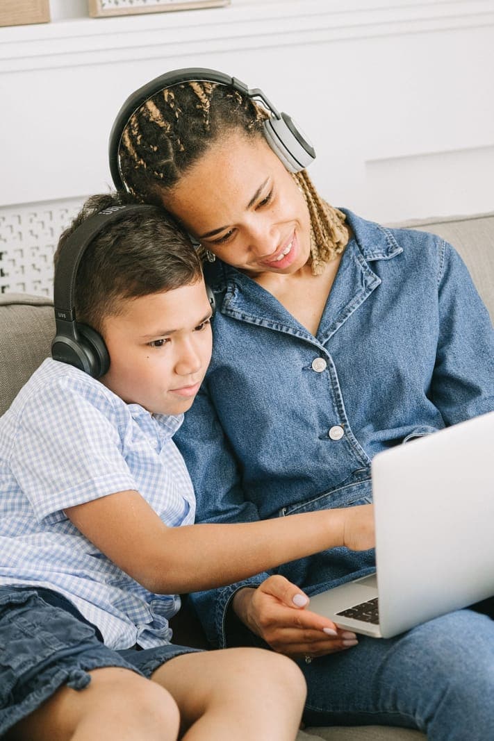 A woman and child sharing a laptop while wearing headphones