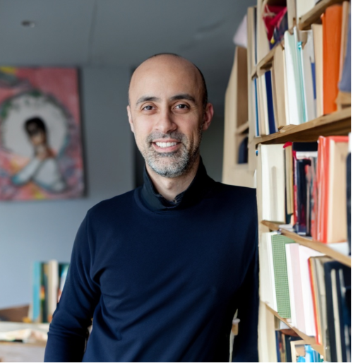 Image of a man in a navy blue shirt standing next to a book shelf