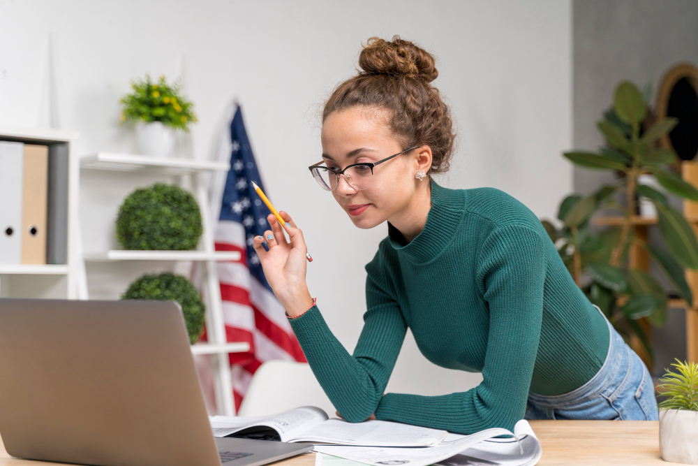 Girl leaning on desk over a computer with American flag in background.