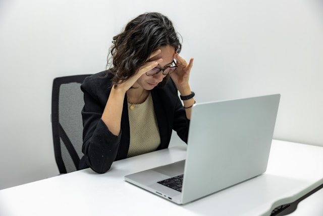 image of a woman in business attire sitting a desk with hands to temples in frustration