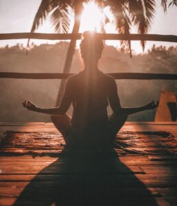 Woman sitting down mediating in the sunset overlooking a forest.