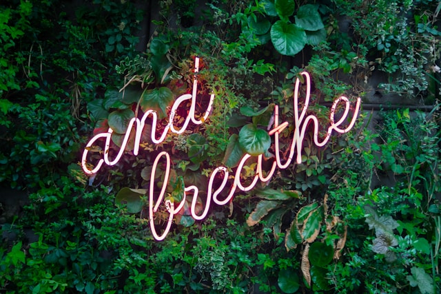 Neon sign against a wall of plants that spells and breathe